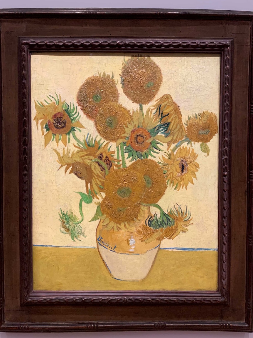 The painting is of yellow flowers in a timber frame, hanging on the wall.