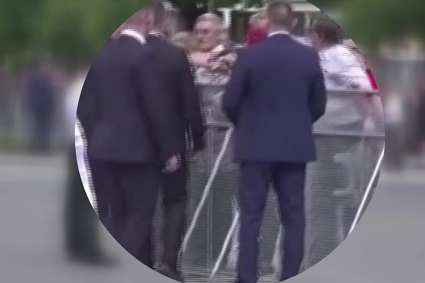 Screengrab of a three men in suits in a crowd in an unblurred circle, with blurring outside the circle.