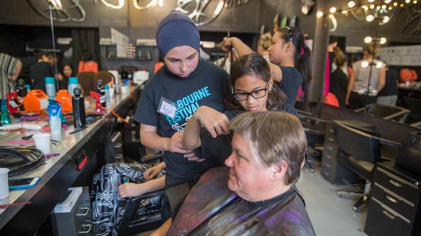Two schoolgirls cut a womans hair in a busy Melbourne salon.