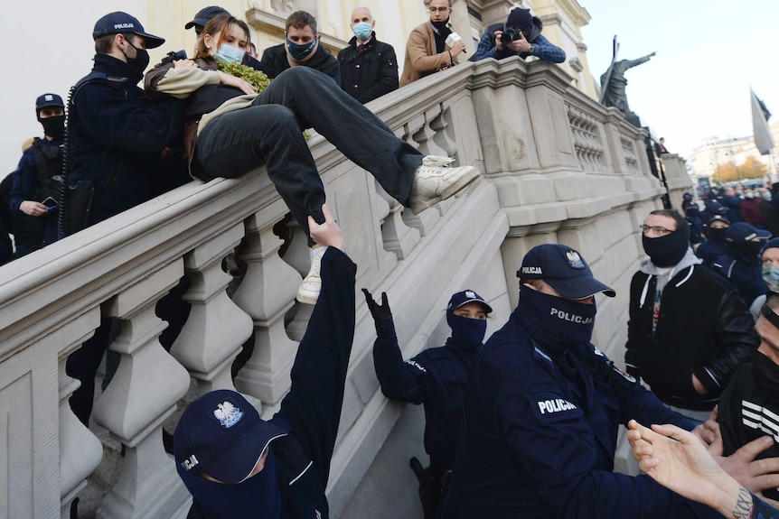 A woman is seen being passed by police officers down a set of stairs. About 10 police officers help as photographer captures it