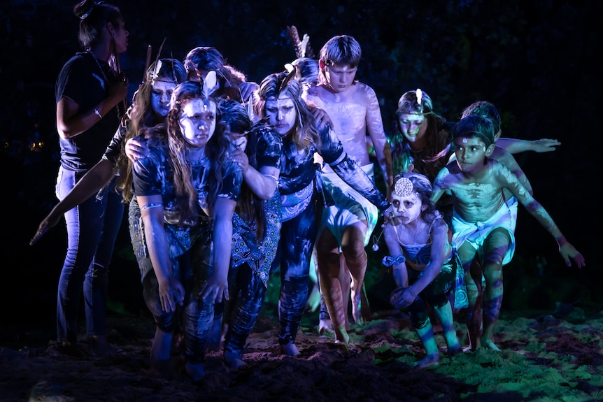 Young indigenous dancers painted in ochre dancing in a tight huddle with stage lights