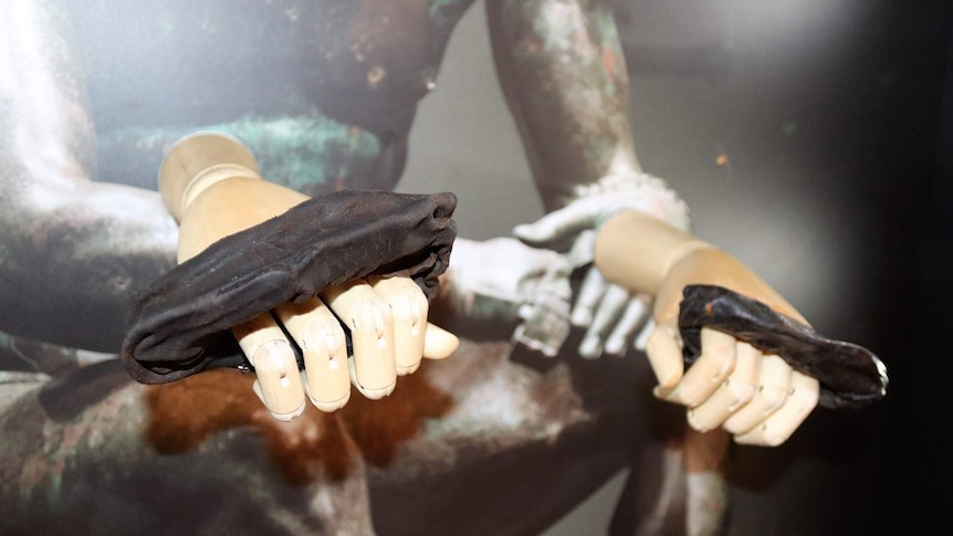 Weathered padded leather straps sit displayed on wooden mannequin hands