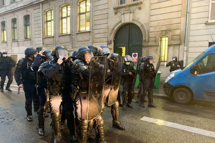 A group of riot police with shields stand in a Paris street.