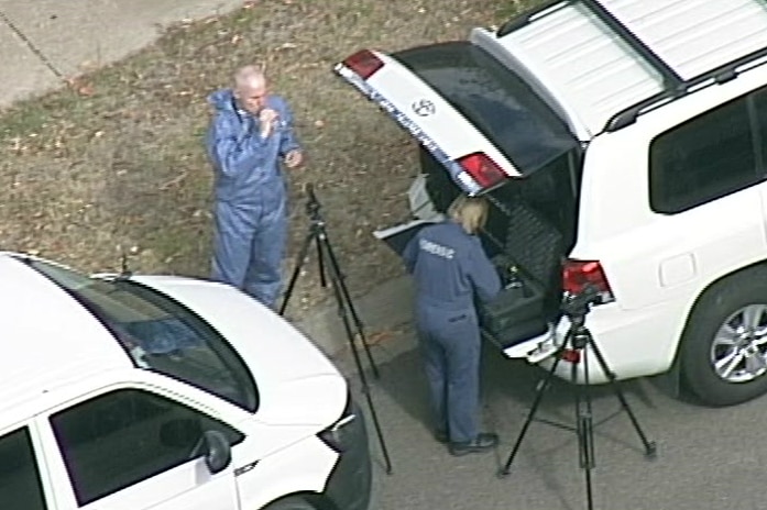 Forensic police officers stand by two tripods and two vans at the crime scene.