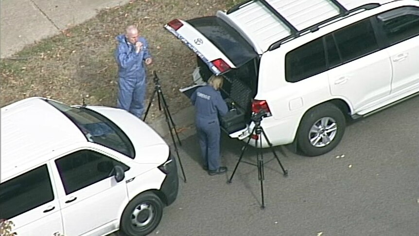 Forensic police officers stand by two tripods and two vans at the crime scene.