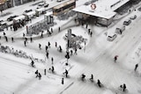An overhead view of people walking and on bikes moving at a snow-covered station.