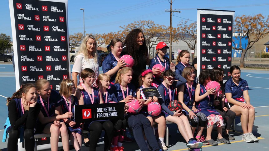 A group of young women in matching blue and pink netball uniforms pose for a team photo, smiling.