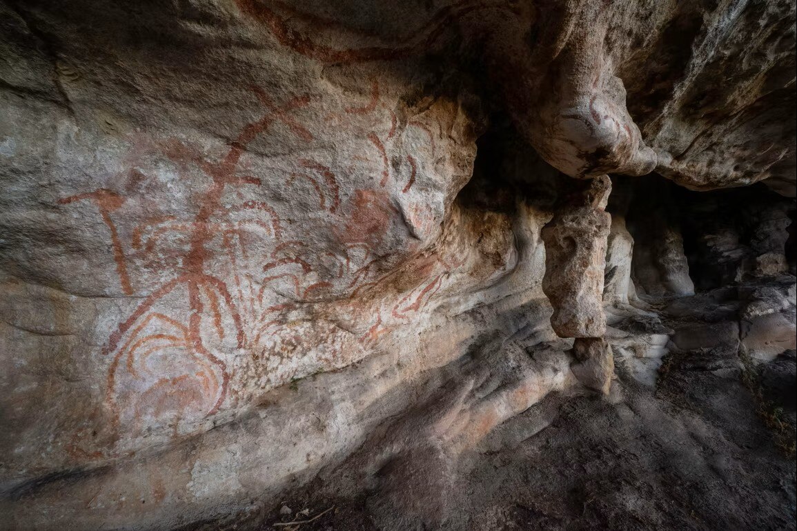 Aboriginal art in red ochre on a rock wall, made up of curved lines.