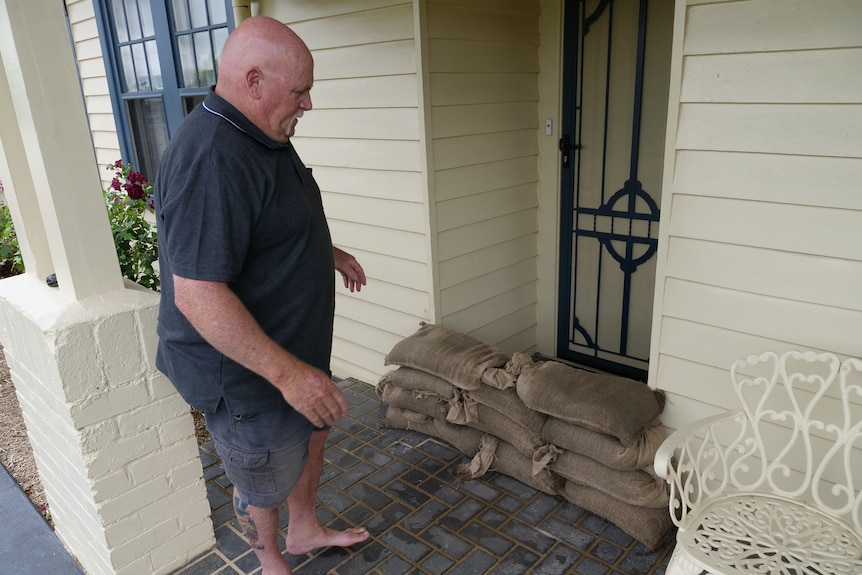 A bald man standing in front of sandbags outside the door to a house
