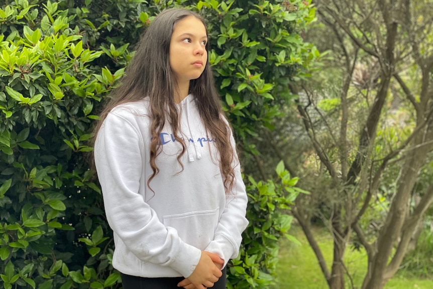 Scarlett Magnanini looks to the side while standing in front of a green leafy bush.