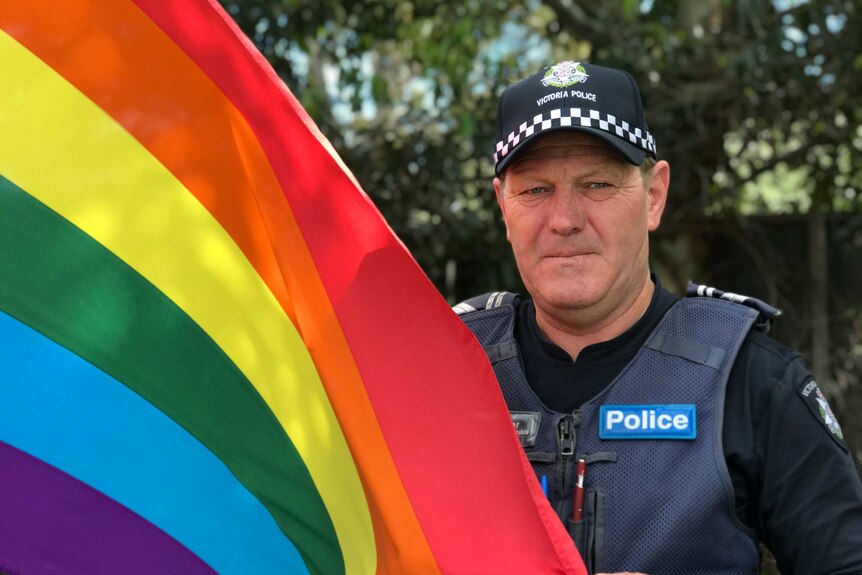 A policeman holds a rainbow flag.