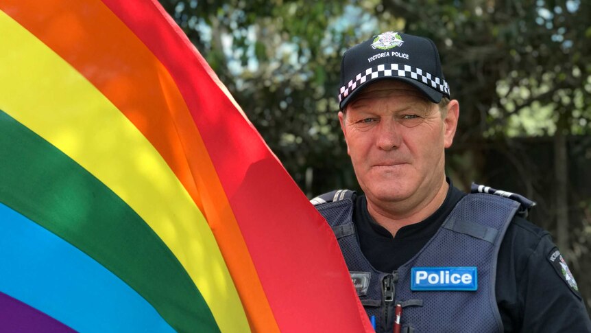 A policeman holds a rainbow flag.