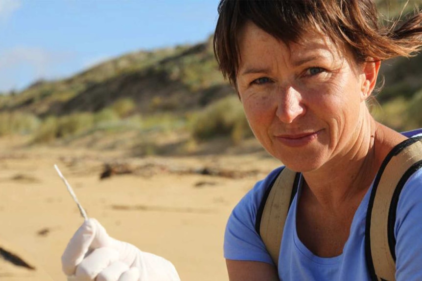 Volunteer Colleen Hughson holding a the plastic pipe from a cotton bud, with beach behind her.