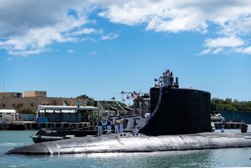 A submarine pulls in to a harbour. 