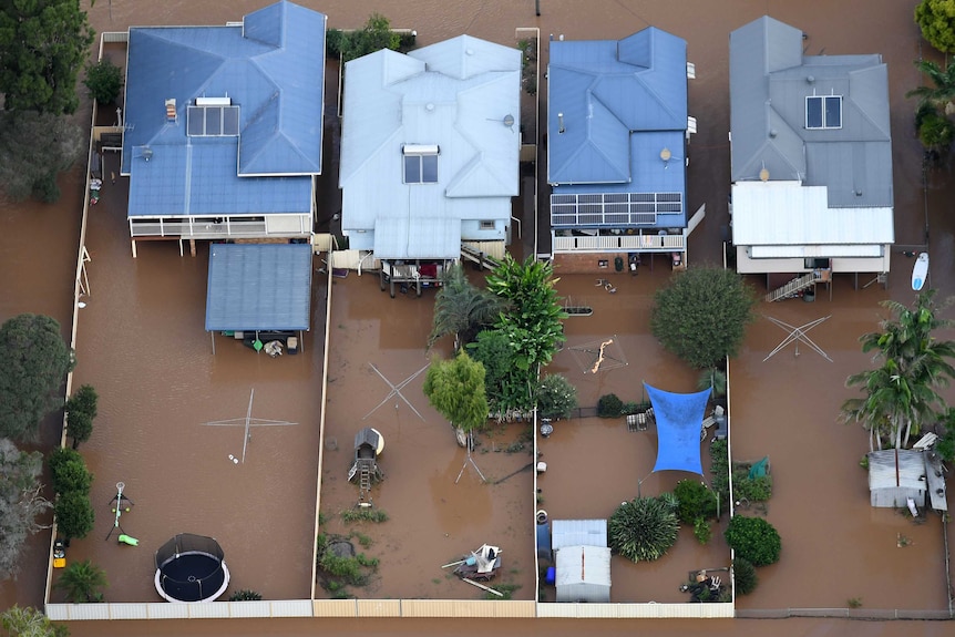 An aerial photograph of flood waters engulfing four houses in the center of Lismore.