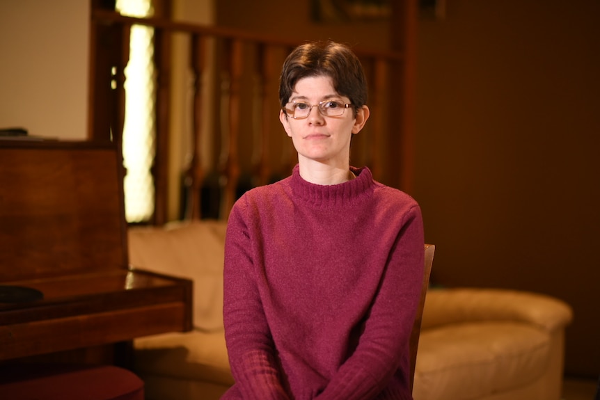 A young white woman with short brown hair and glasses. She's wearing a maroon jumper