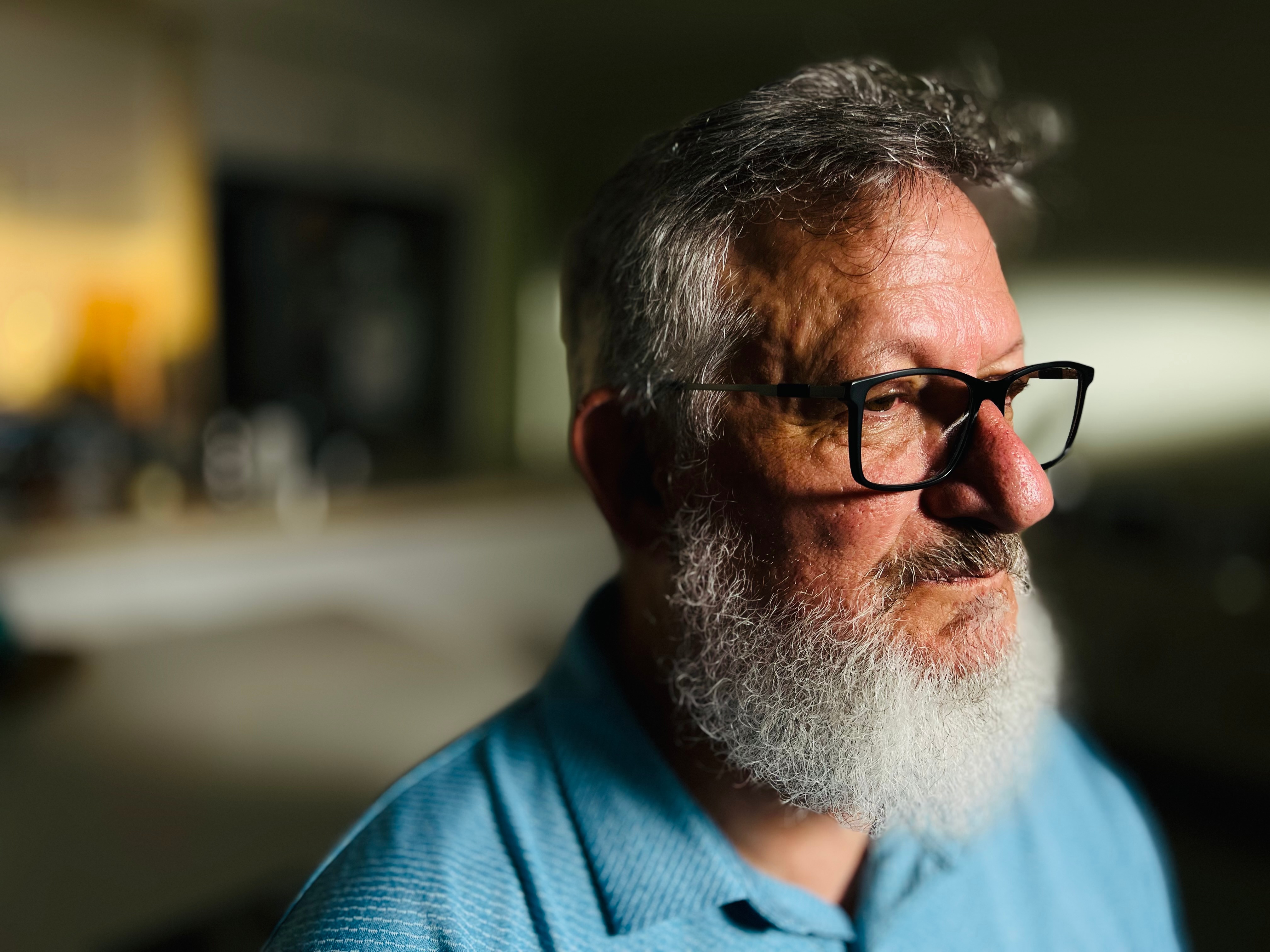 a man with a thick grey beard and hair, wearing black reading glasses