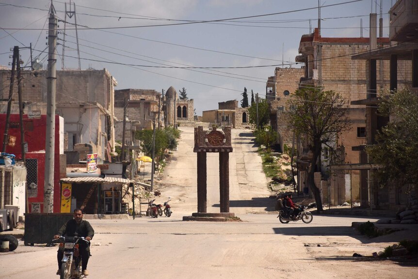 Momument and buildings in Khan Sheikhoun, Syria, with man riding motorbike in foreground.