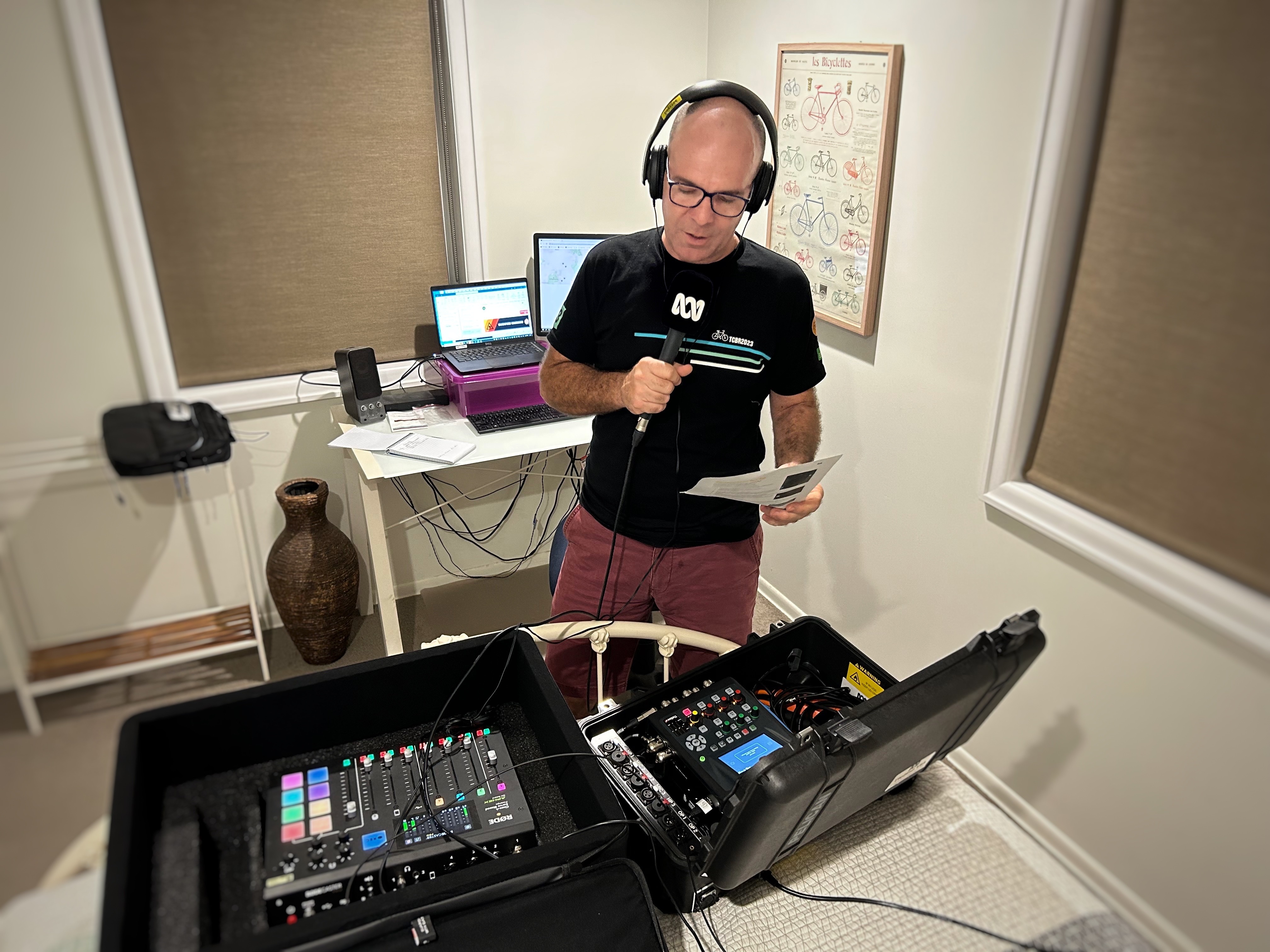 A man with headphones on speaks into a microphone with two large audio panels in front of him