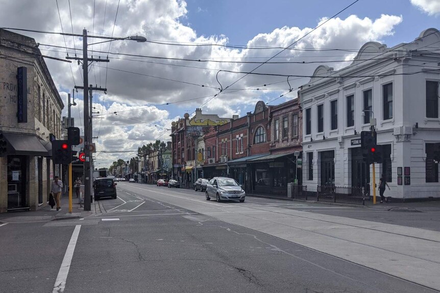 An intersection of Brunswick Street and Johnston Street with one car stopped at lights on a bright day.