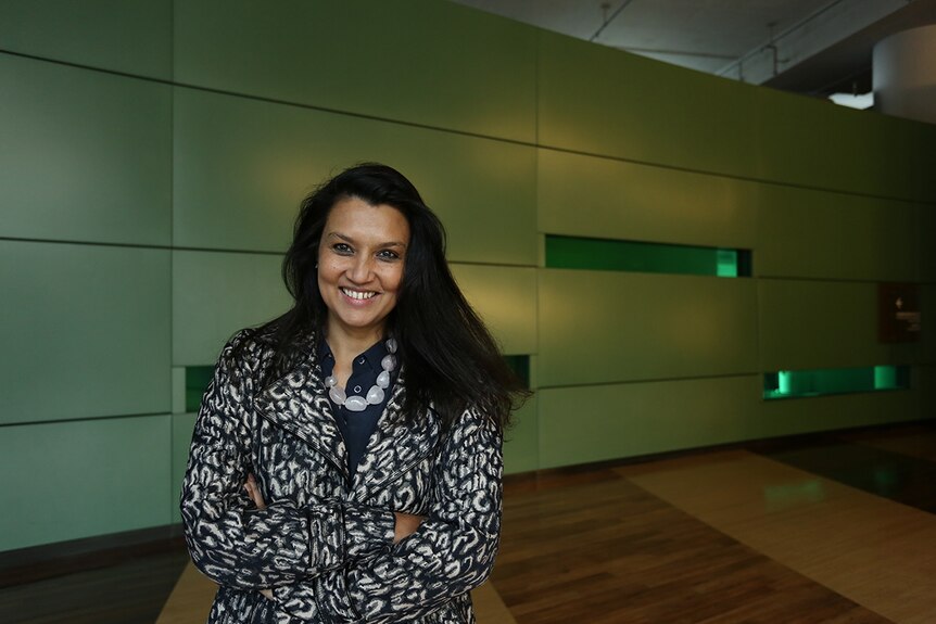Colour photograph of Suhanya Raffel, head of M+ art museum, standing in a room with green walls and wooden floor boards.