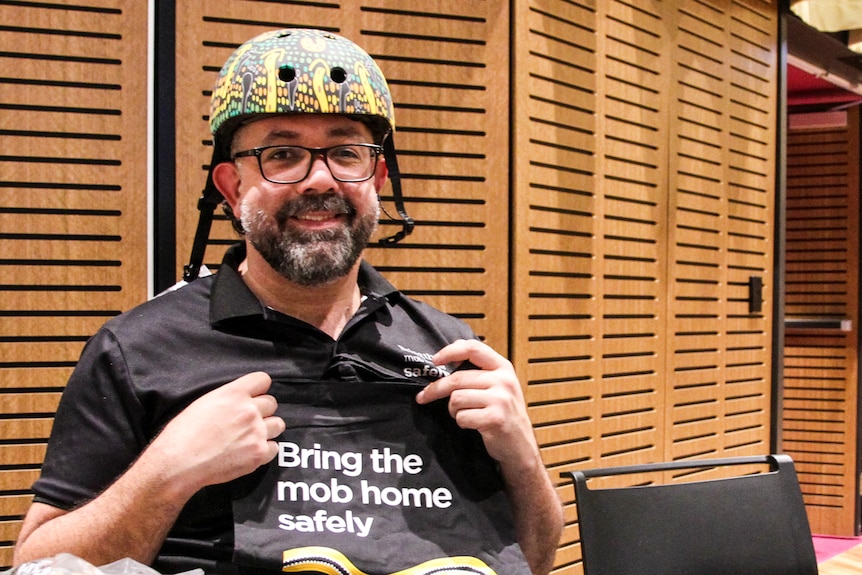 A man wearing a bicycle helmet smiles at the camera