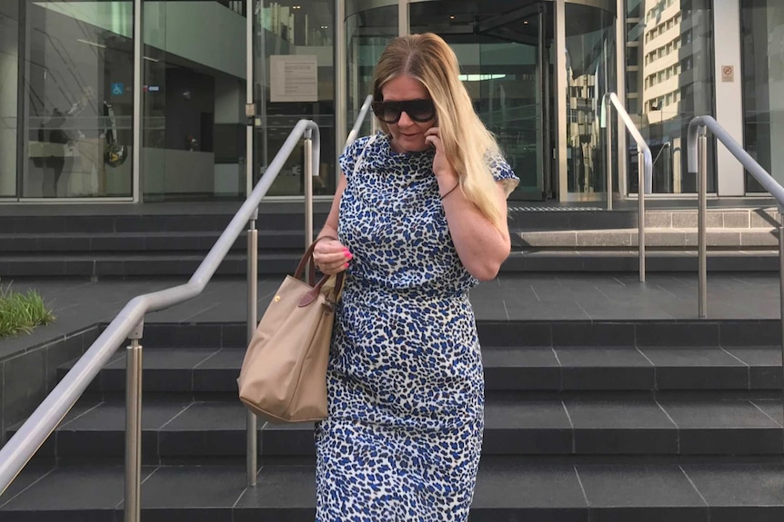 A woman wearing a purple top and black pants walks on a sidewalk outside the Perth court building.