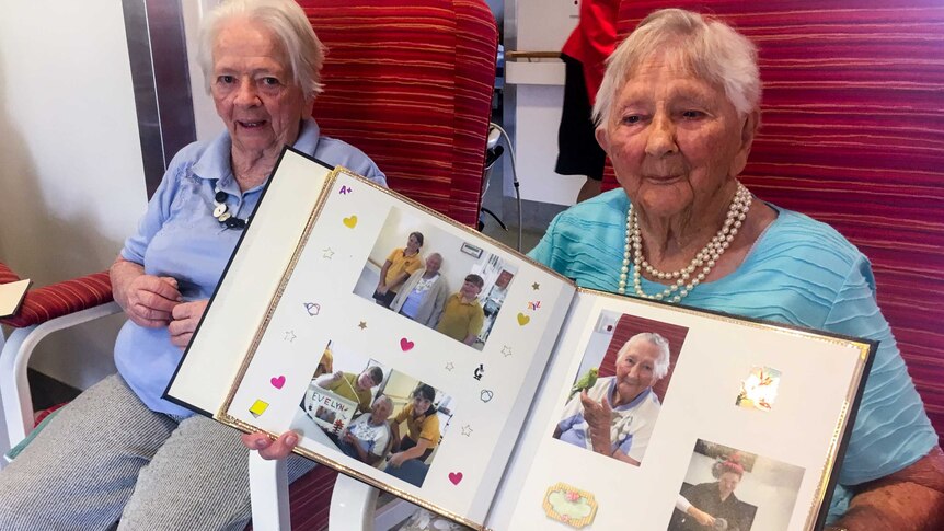 Two older women sitting in chairs holding a photo album