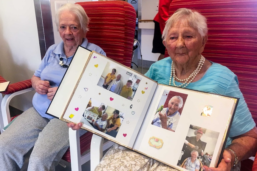 Two older women sitting in chairs holding a photo album