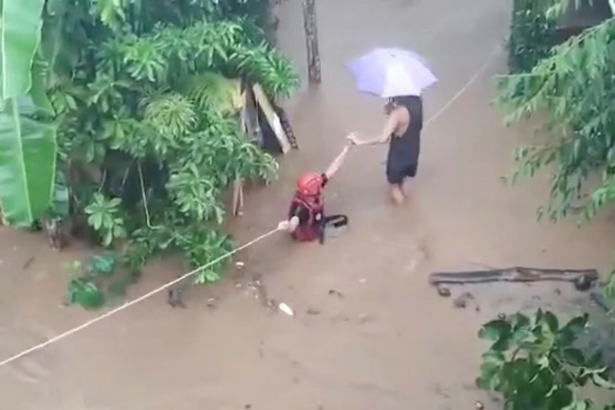 A birds-eye-view photo shows two people holding onto ropes in flooded muddy waters