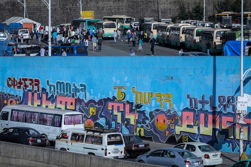 Passengers look for buses at a station, while vehicle drivers sit in traffic nearby.