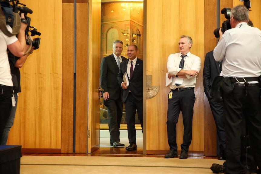 Josh Frydenberg walks into a room full of reporters holding a budget folder.