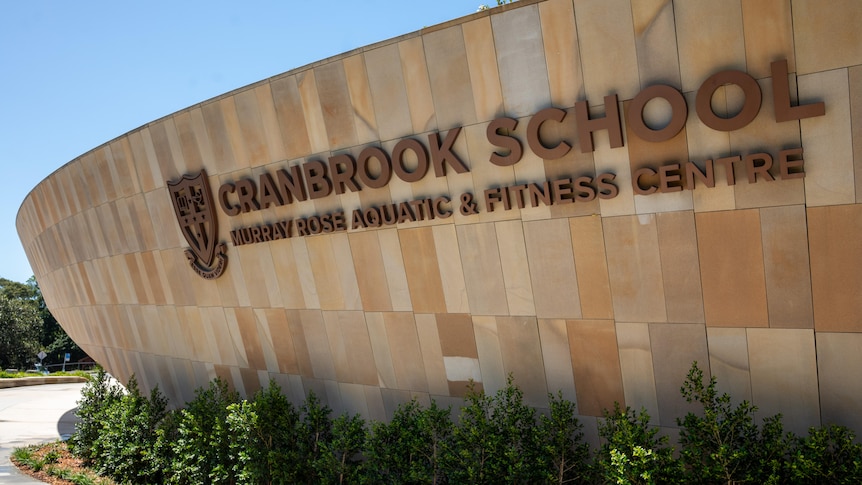 A curved sandstone wall with the words 'Cranbrook School  Murray Rose Aquatic & Fitness Centre'.