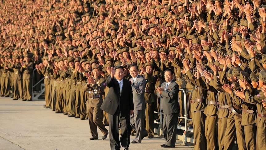 Kim Jong Un wearing a western-style suit walks past a crowd of applauding soldiers