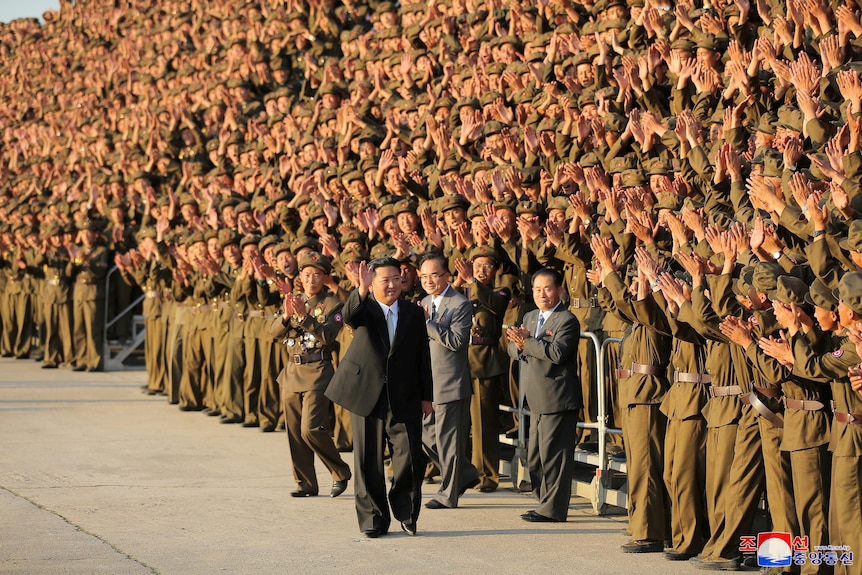 Kim Jong Un wearing a western-style suit walks past a crowd of applauding soldiers