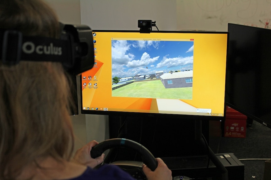 A woman wears headset sitting in front of computer screen with driving simulator