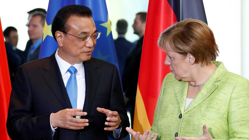 Angela Merkel and Li Keqiang gesture with both hands open in front of a German and EU flag