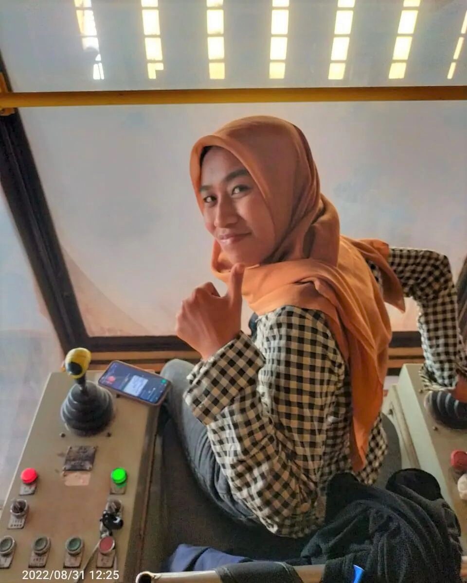 A woman at work sits in a crane and smiles at a camera.