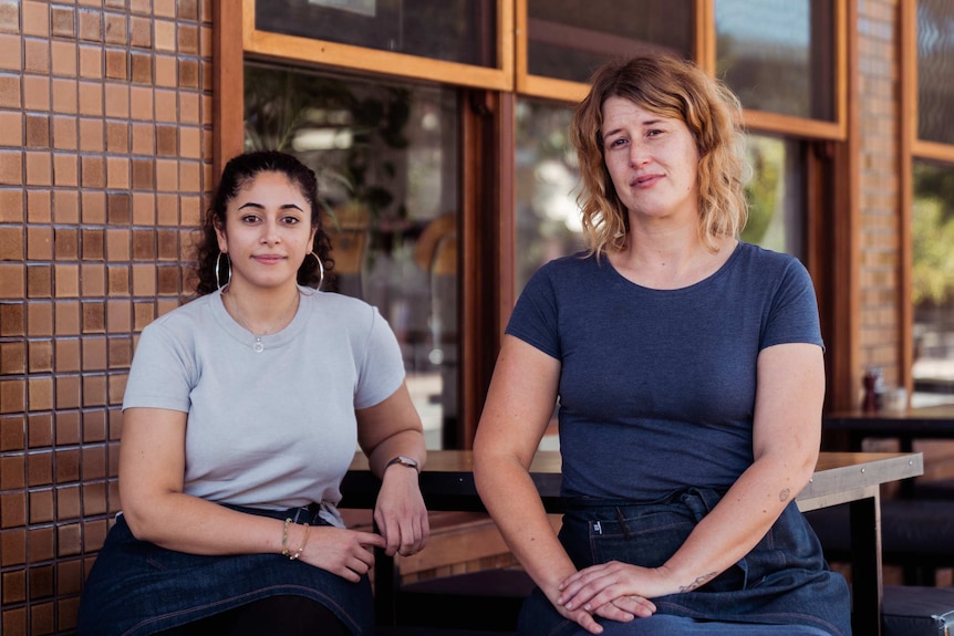 Lydia and Becca lean on a table outside the bakery.