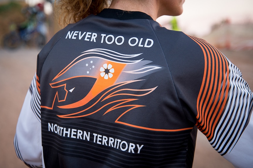 The back of a female BMX rider's shirt with a graphic representation of a helmet and the words 'Never Too Old' written above it.