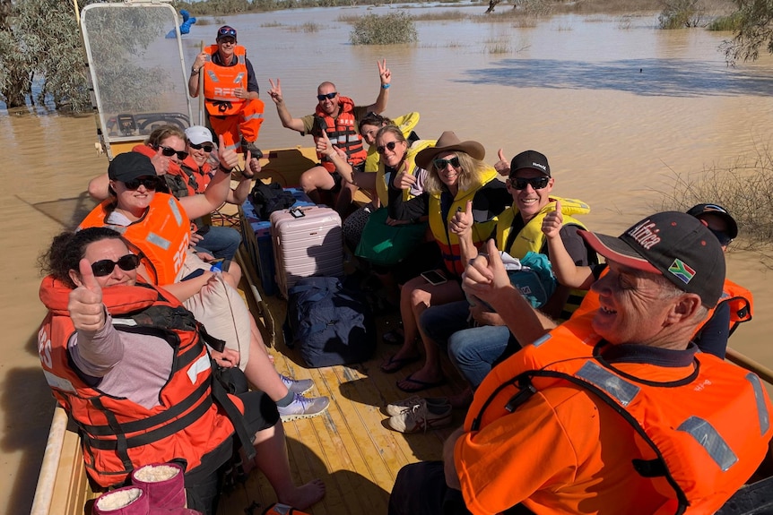 A boatful of people wearing orange vest with luggage in floodwaters.