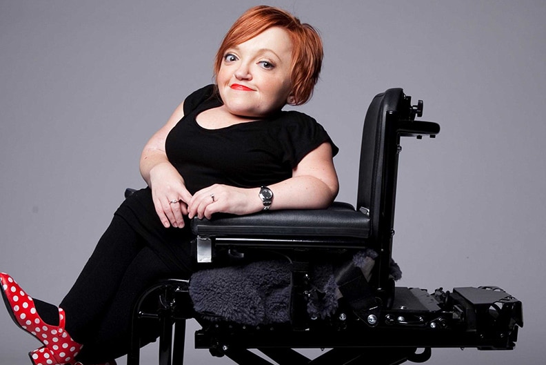 A woman with red hair poses for a photo while sitting in a wheelchair.