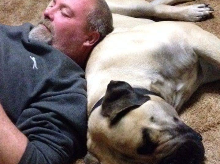 A man lays with his head resting on his dog's body.