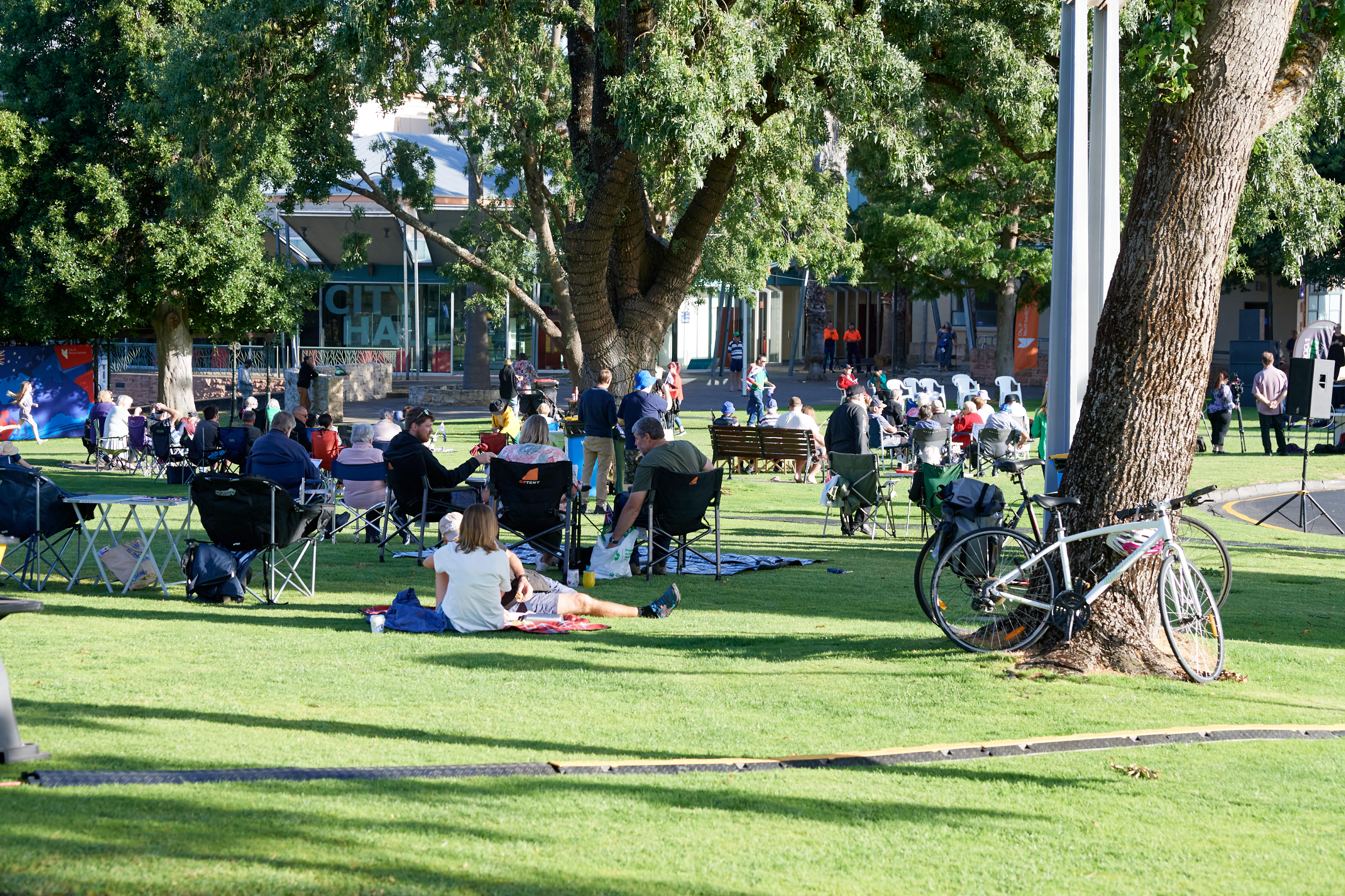 A crowd of people sitting on grass watching a stage. 