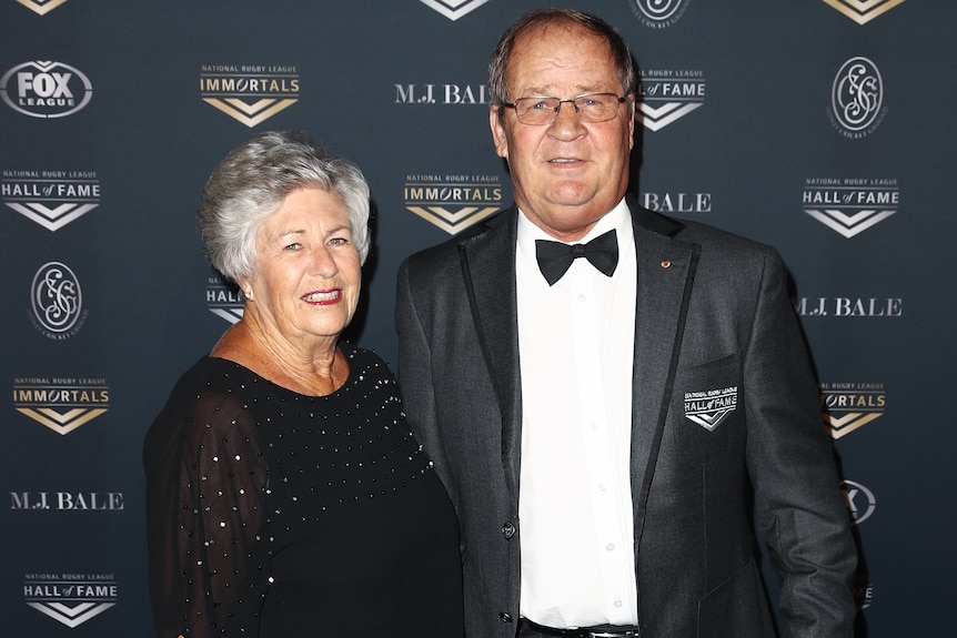 A man wearing a dinner suit poses for a photo alongside his wife at an NRL function in 2018.