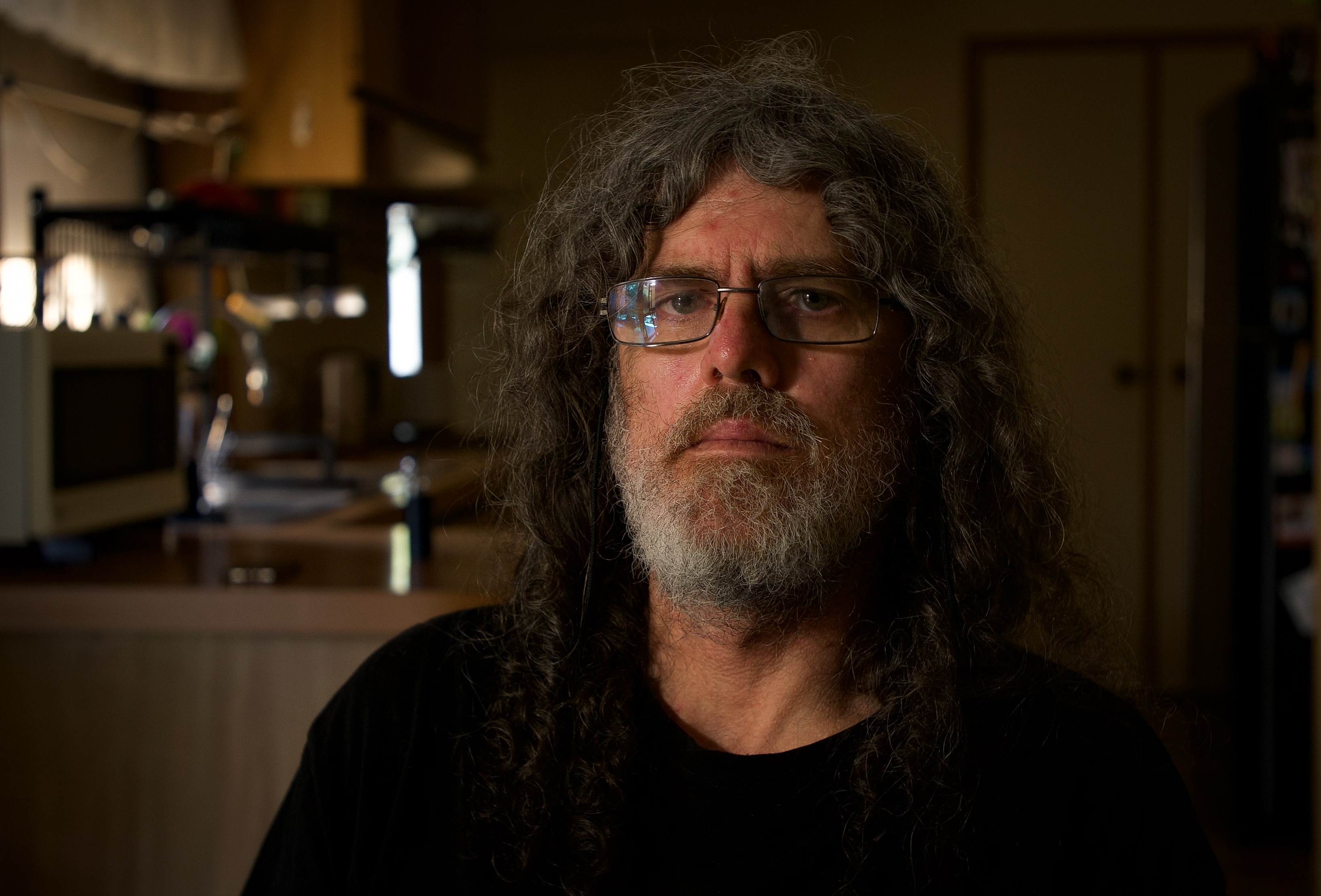 Man with long hair and a beard wearing glasses and a black top.