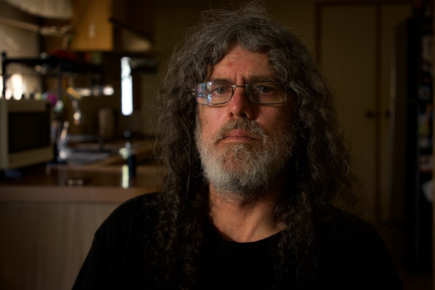 Man with long hair and a beard wearing glasses and a black top.
