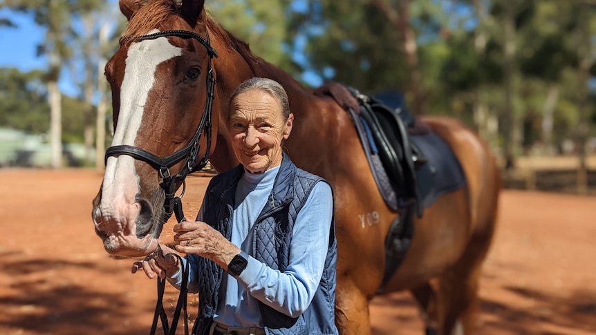 Woman in her 80s smiling and standing with chestnut coloured horse