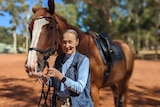 Woman in her 80s smiling and standing with chestnut coloured horse