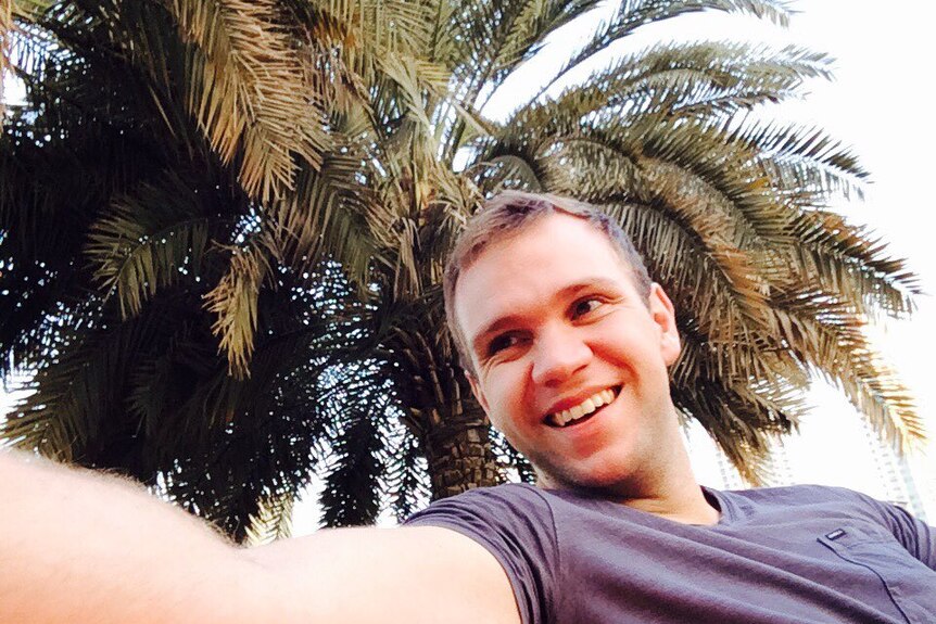 A smiling man taking a selfie in front of a palm tree.